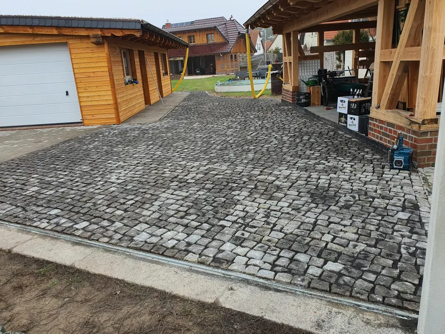 Einfahrt aus Naturstein-Kleinpflaster im Bogenverband vor einem Holzhaus